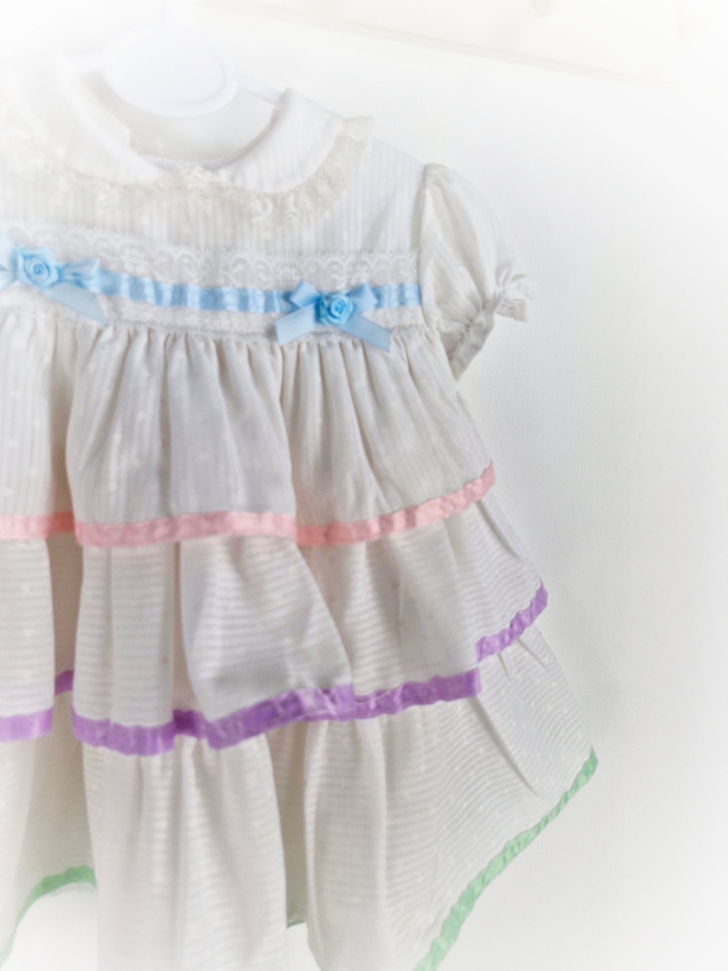 12 months. White dress with pastel ribbons and lace.