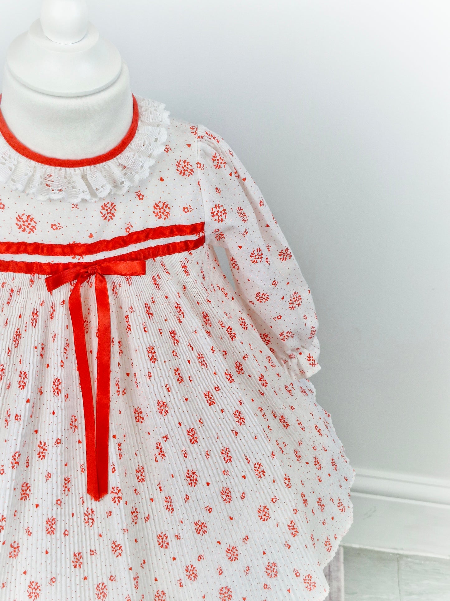 2 years. White dress with mini pleats, red details and ribbon and white lace collar.
