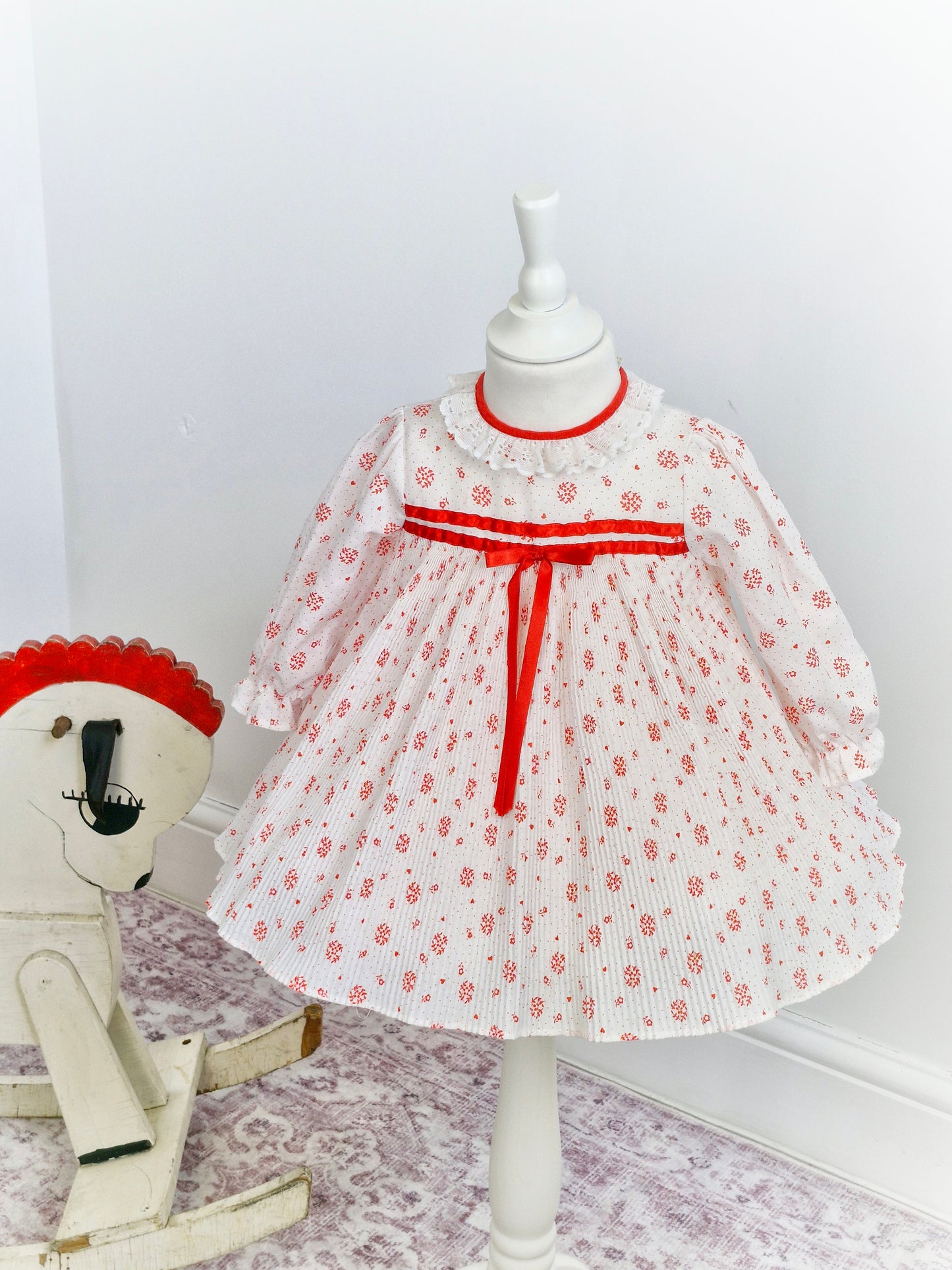 2 years. White dress with mini pleats, red details and ribbon and white lace collar.