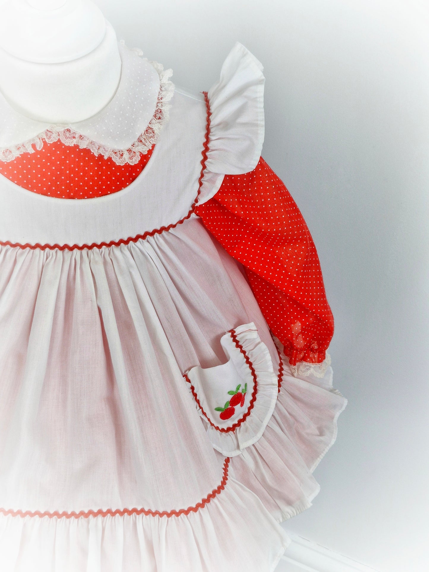 2 years. Red polka dot Bryan with Peter Pan collar and white pinny with flutter sleeves and cherries on pocket.