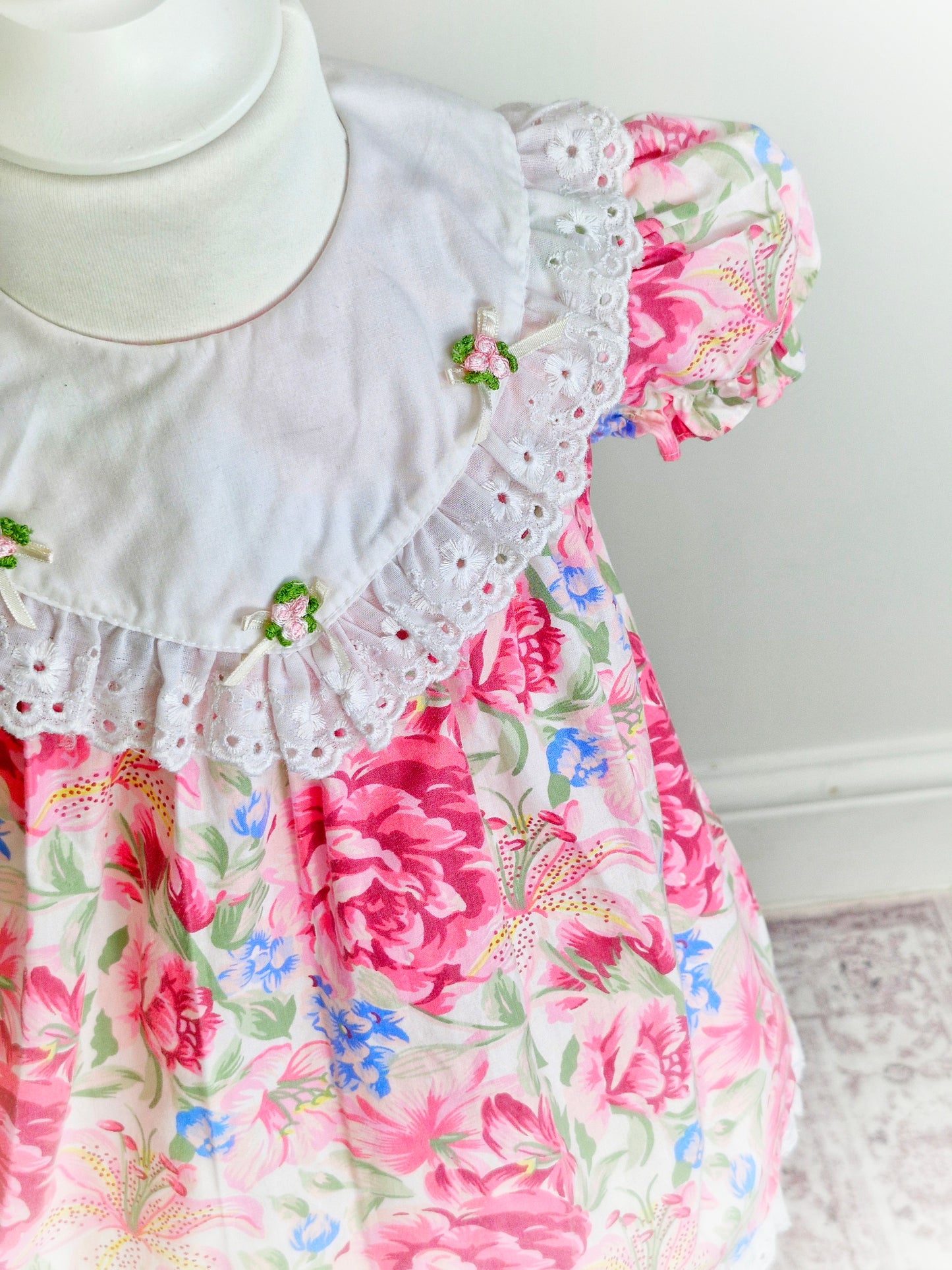 2 years. Pink vintage floral dress with white bib, rosettes and broderie anglais trim