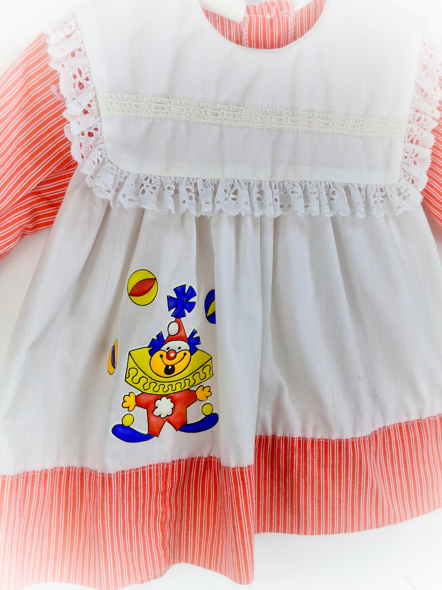12 months. White dress with red sleeves and hem, lace trim on bib and clown applique