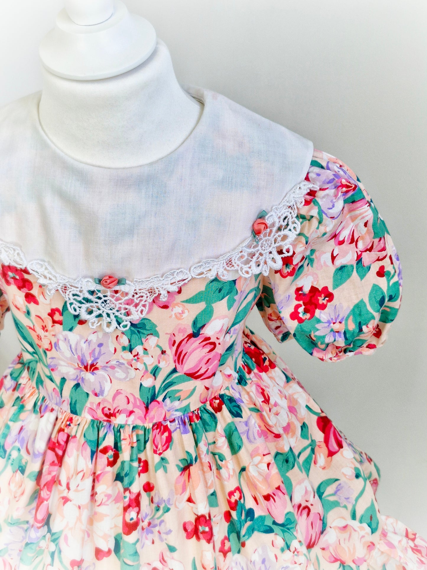 3 years. Peach vintage dress with large flower print, white bib with lace trim and 3 rosettes. Bonnie Jean.