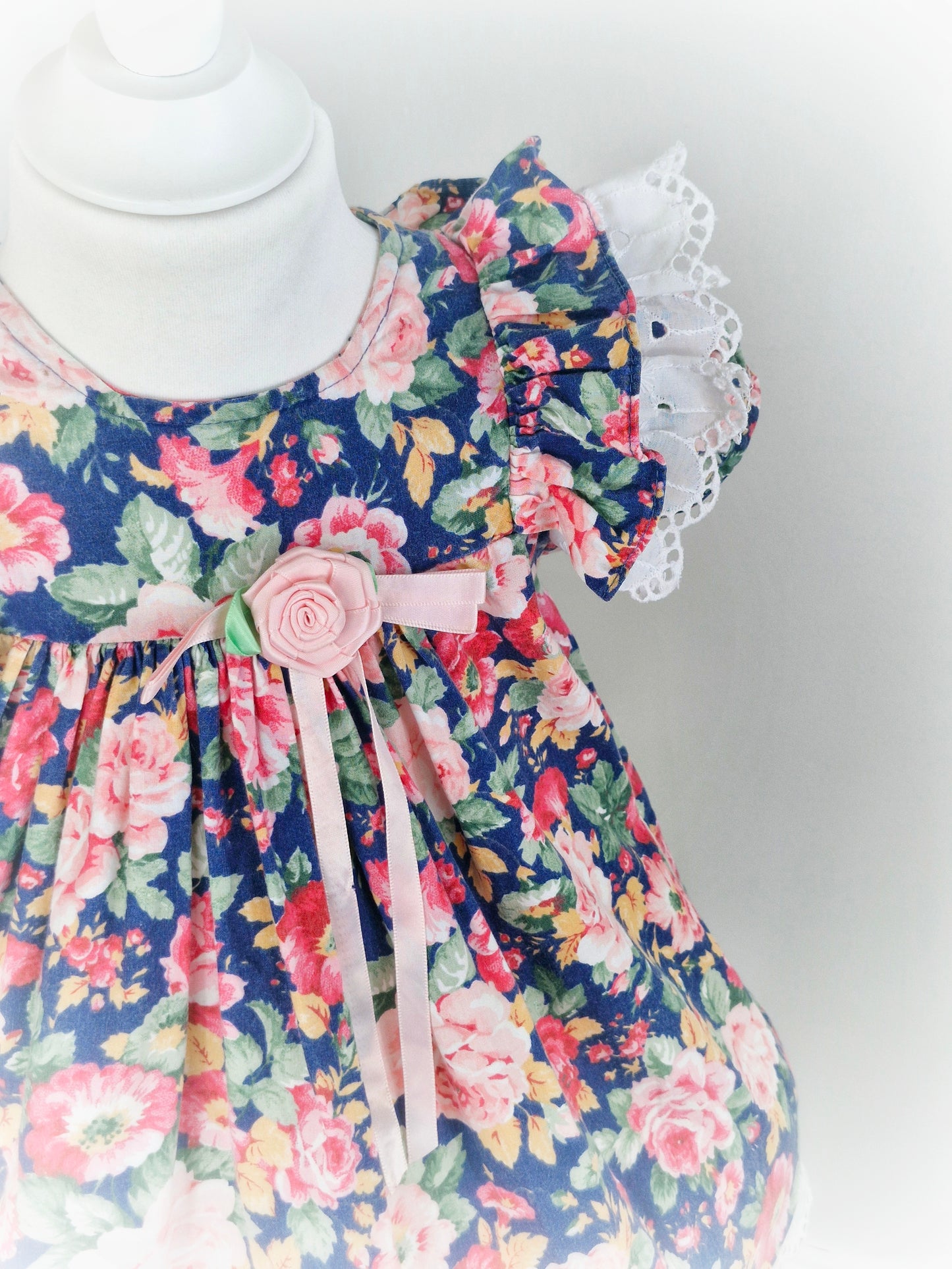 2 years. Navy and pink floral dress with white broderie anglais flutter sleeves and hem from Rare Editions