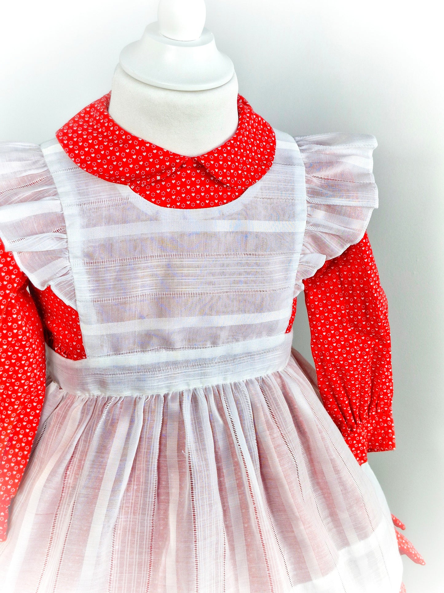 2-3 years. Handmade two-piece, red long sleeve dress with Peter Pan collar and white heart print. White apron with flutter shoulders and tie back.