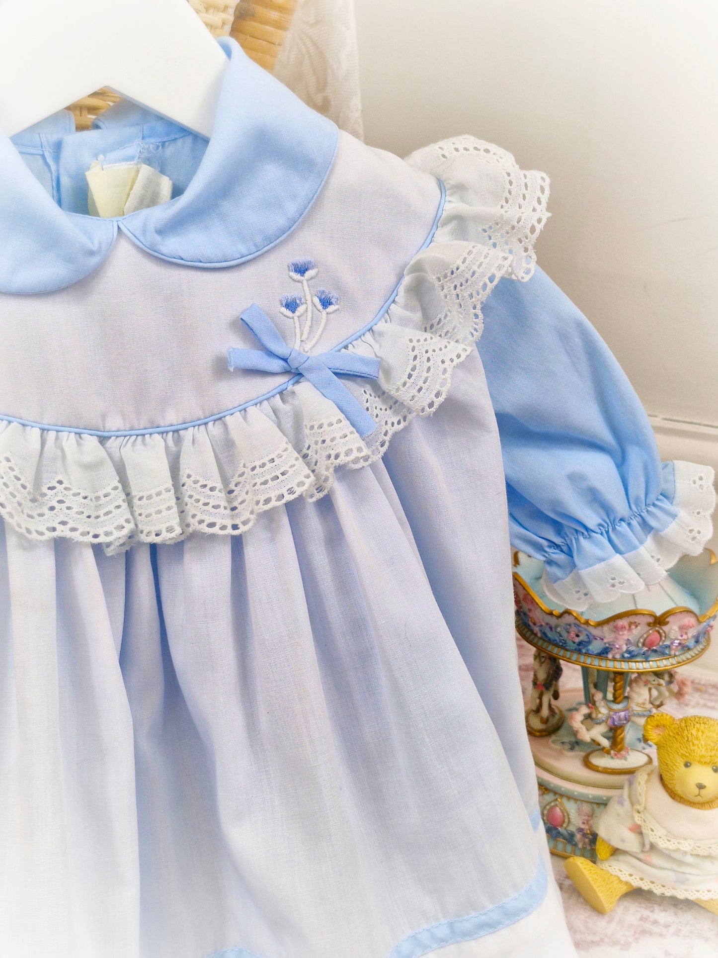 12-18 months. Two piece, blue dress with puff sleeves and Peter Pan collar with white apron, trimmed with white lace and blue embroidered flowers