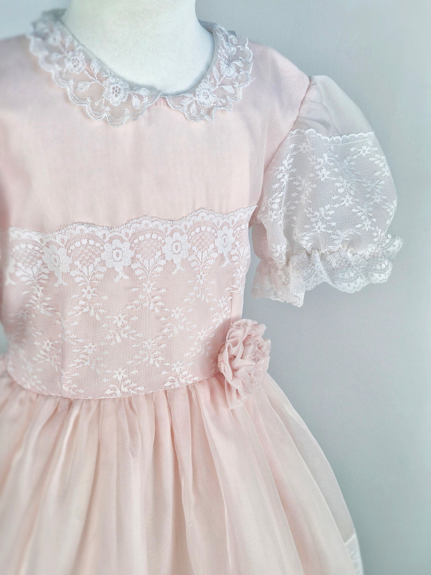7-8 years. Light pink vintage organza dress with puff sleeves, white lace details and a floral accent at the waist.