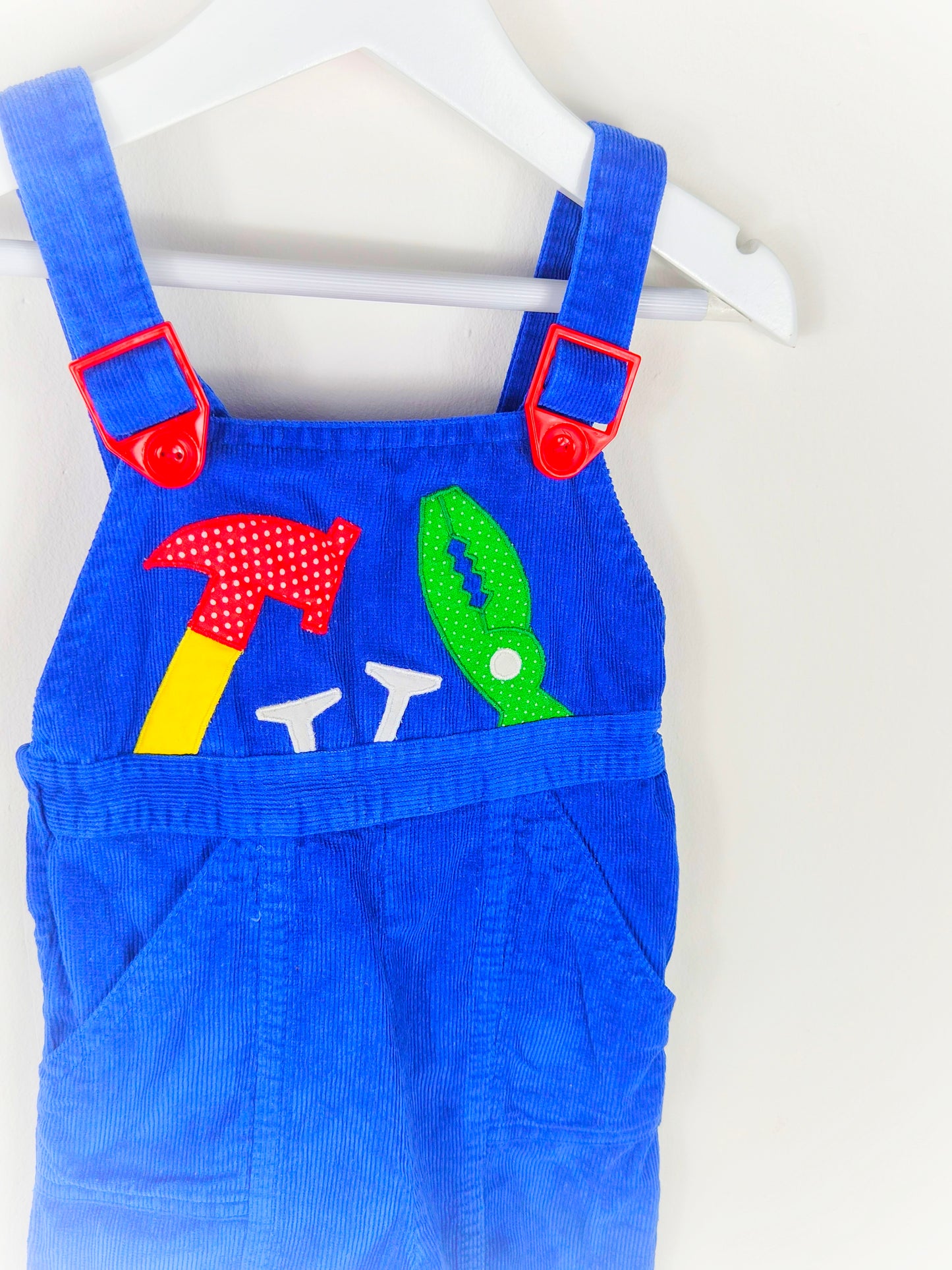 12 months. Blue corduroy dungarees with red adjustable buckles and tools