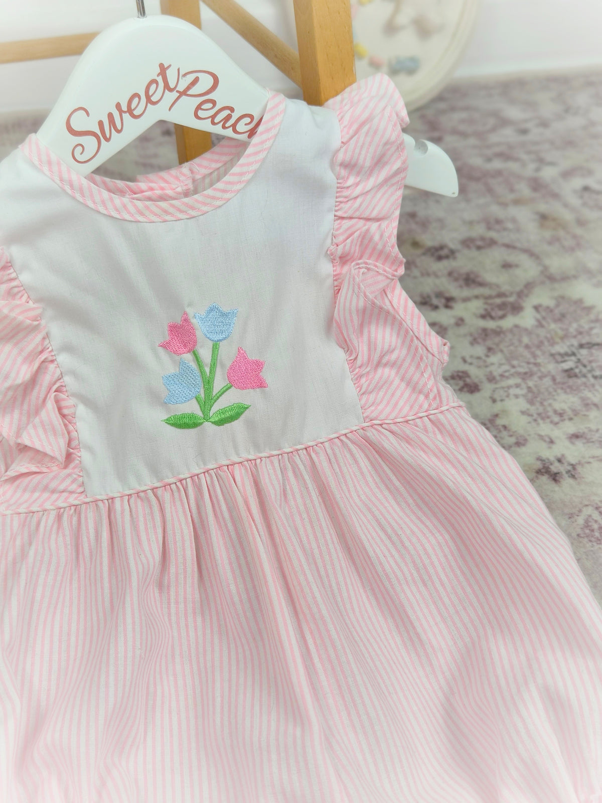 9-12 months. Pink and white striped, sleeveless Alexis romper with frills and embroidered flowers