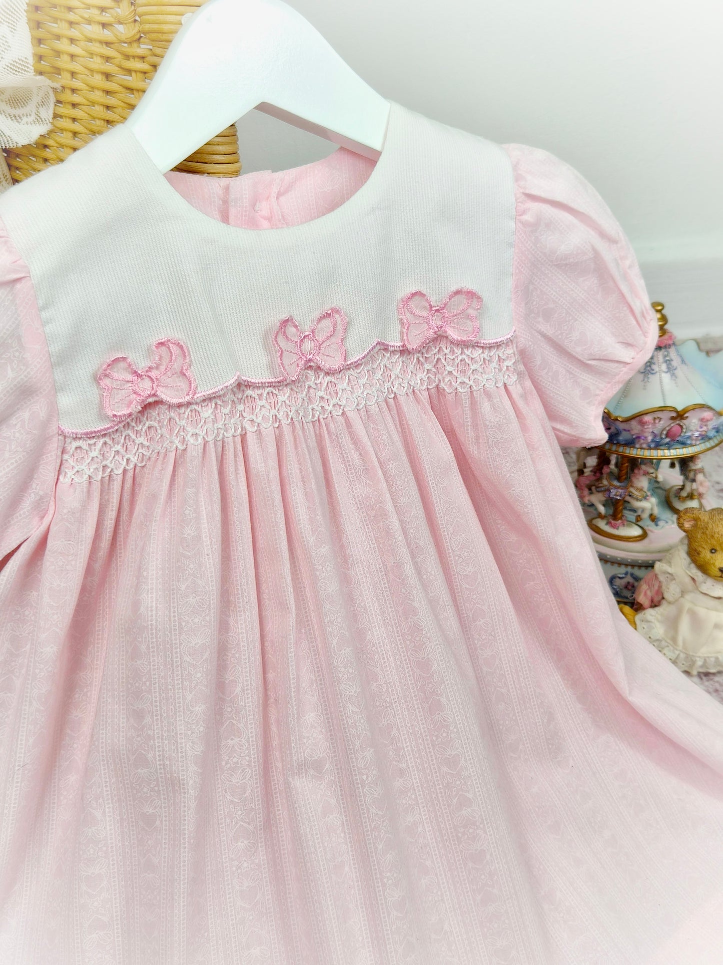 2 years. Pink vintage smocked dress by Maude Wilson with white bib, floral print and three pink bows