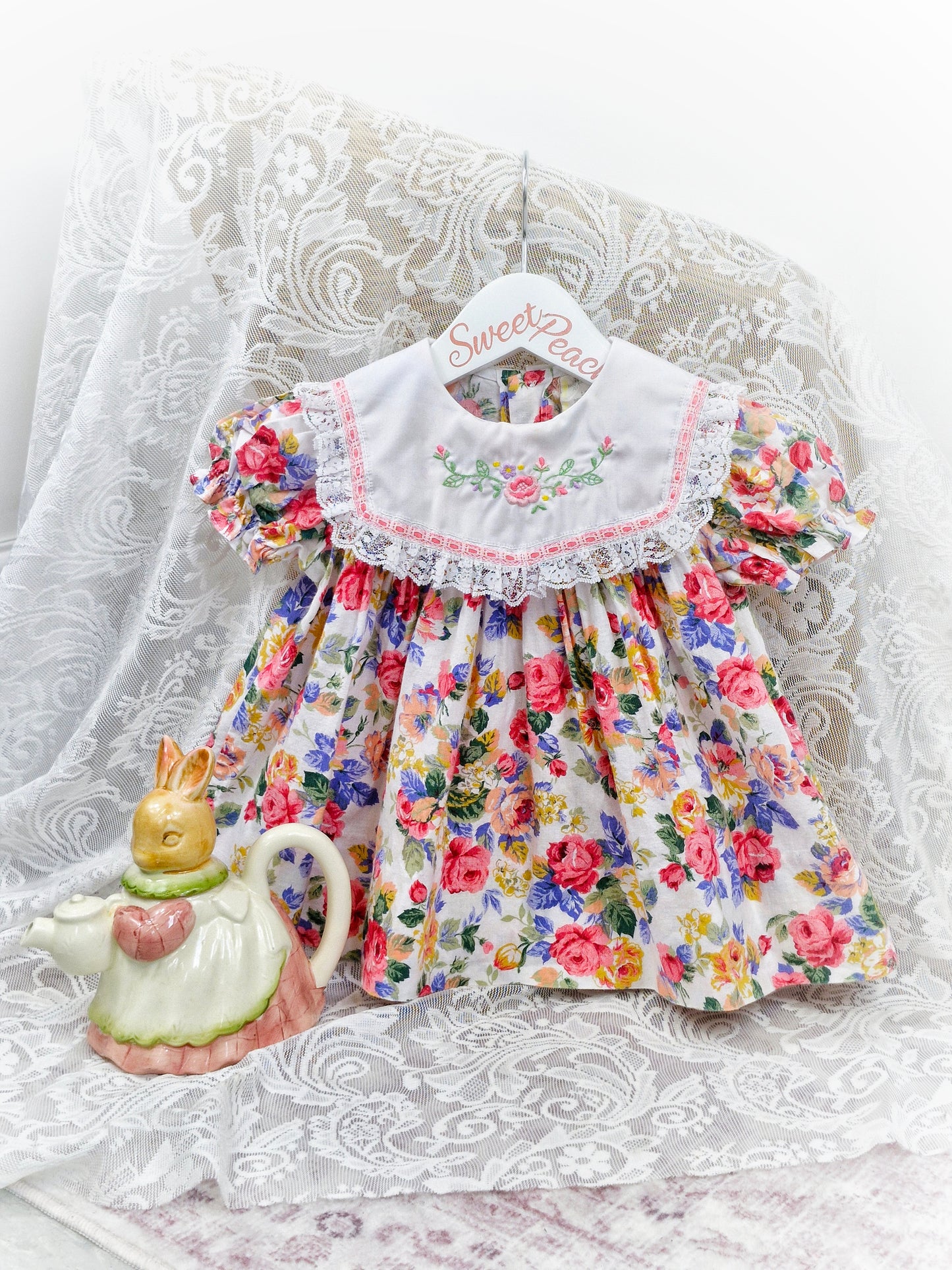9-12 months. Floral dress with white bib embroidered with flowers and finished with lace