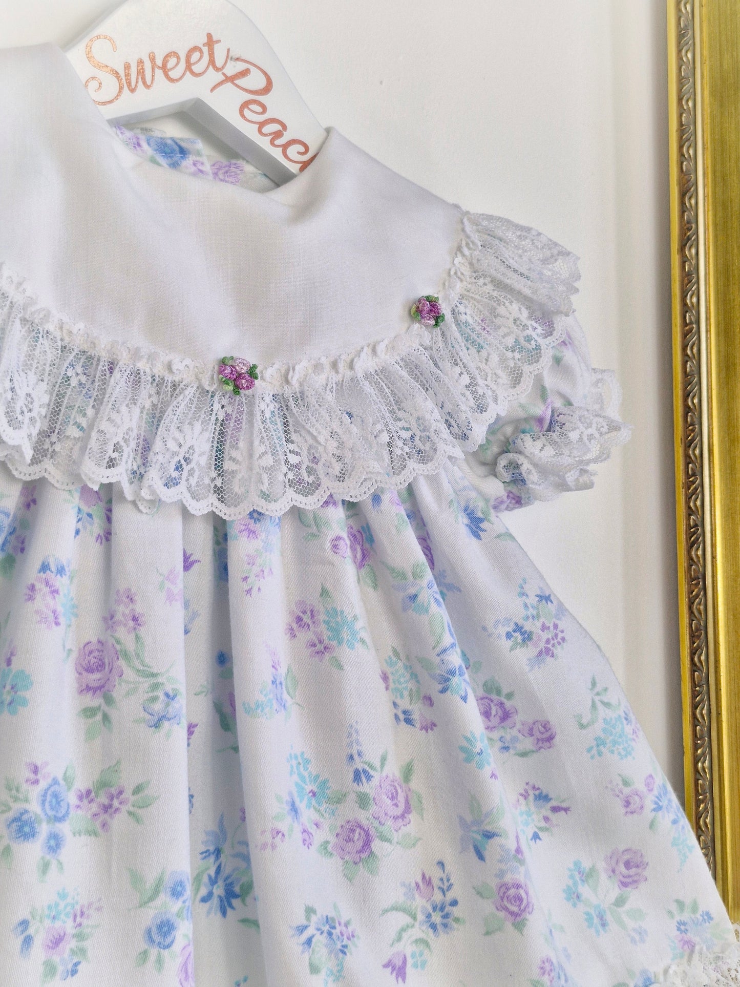 12 months. White Cutest One dress with blue and lilac flowers, lace trim and rosettes on bib