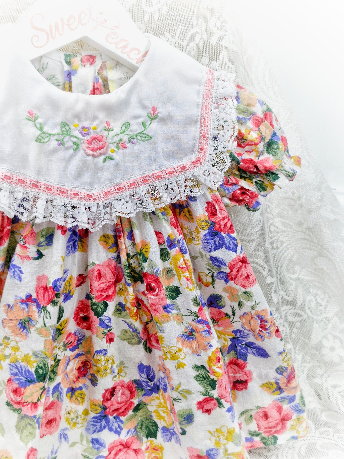 9-12 months. Floral dress with white bib embroidered with flowers and finished with lace