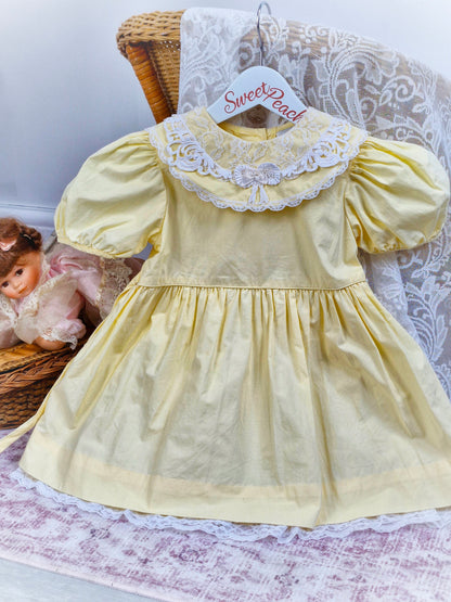 3 years. Lemon dress with white lace and bow on bib. Lace hem.