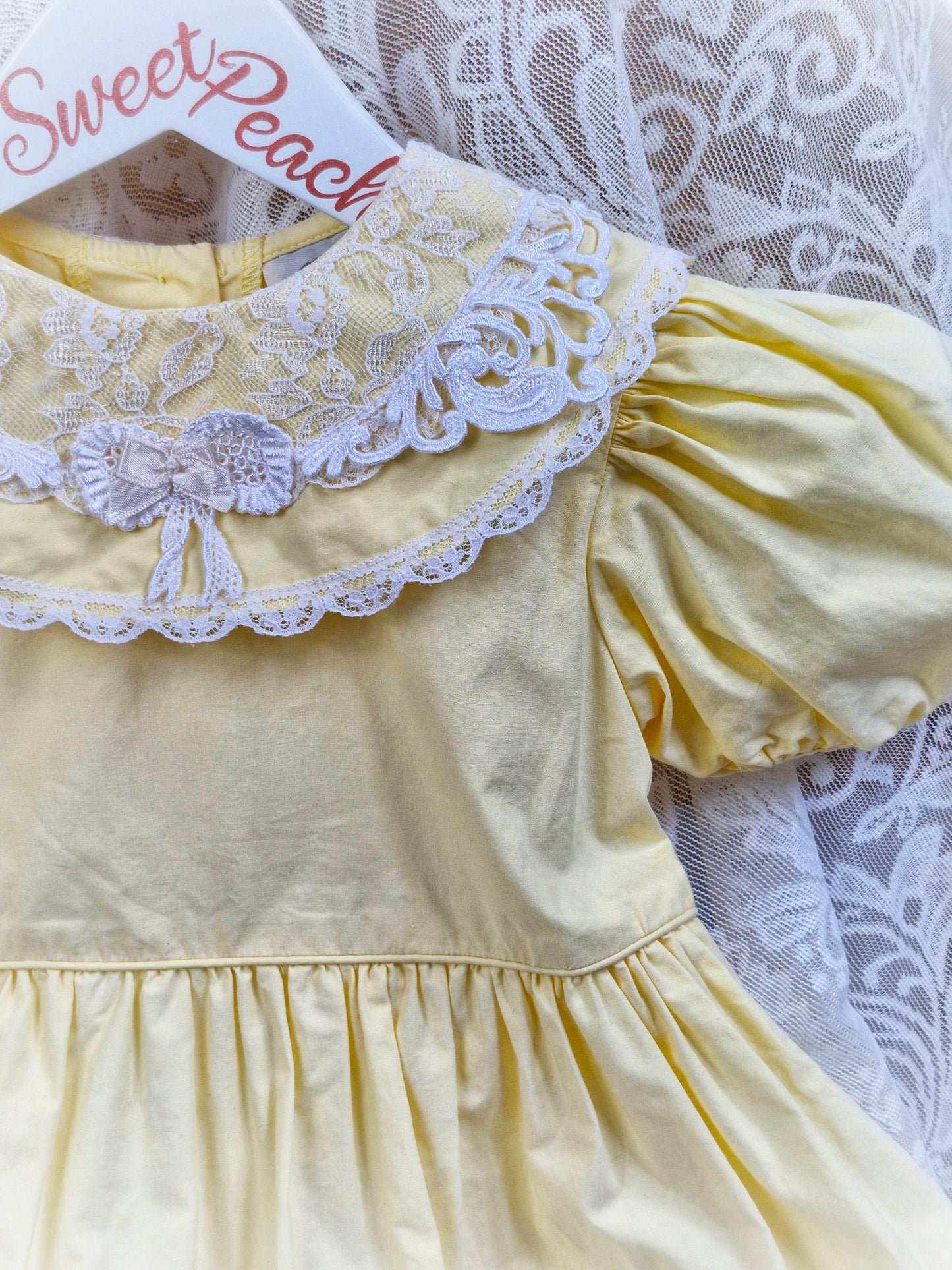 3 years. Lemon dress with white lace and bow on bib. Lace hem.