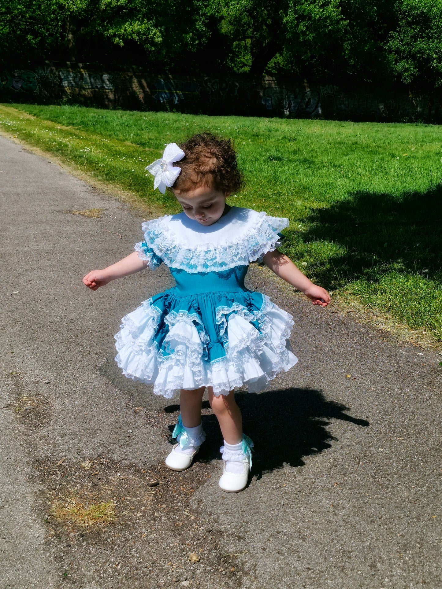 6-12 months. Teal Lid'l Dolly with white ruffles, lace and bib