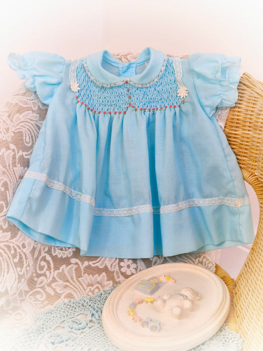 6-9 months. Blue smock dress with pink flowers and white lace details