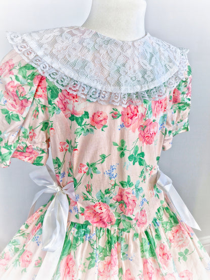 6-7 years. Peach dress with pink flowers, white lace bib and ribbon bows on sides