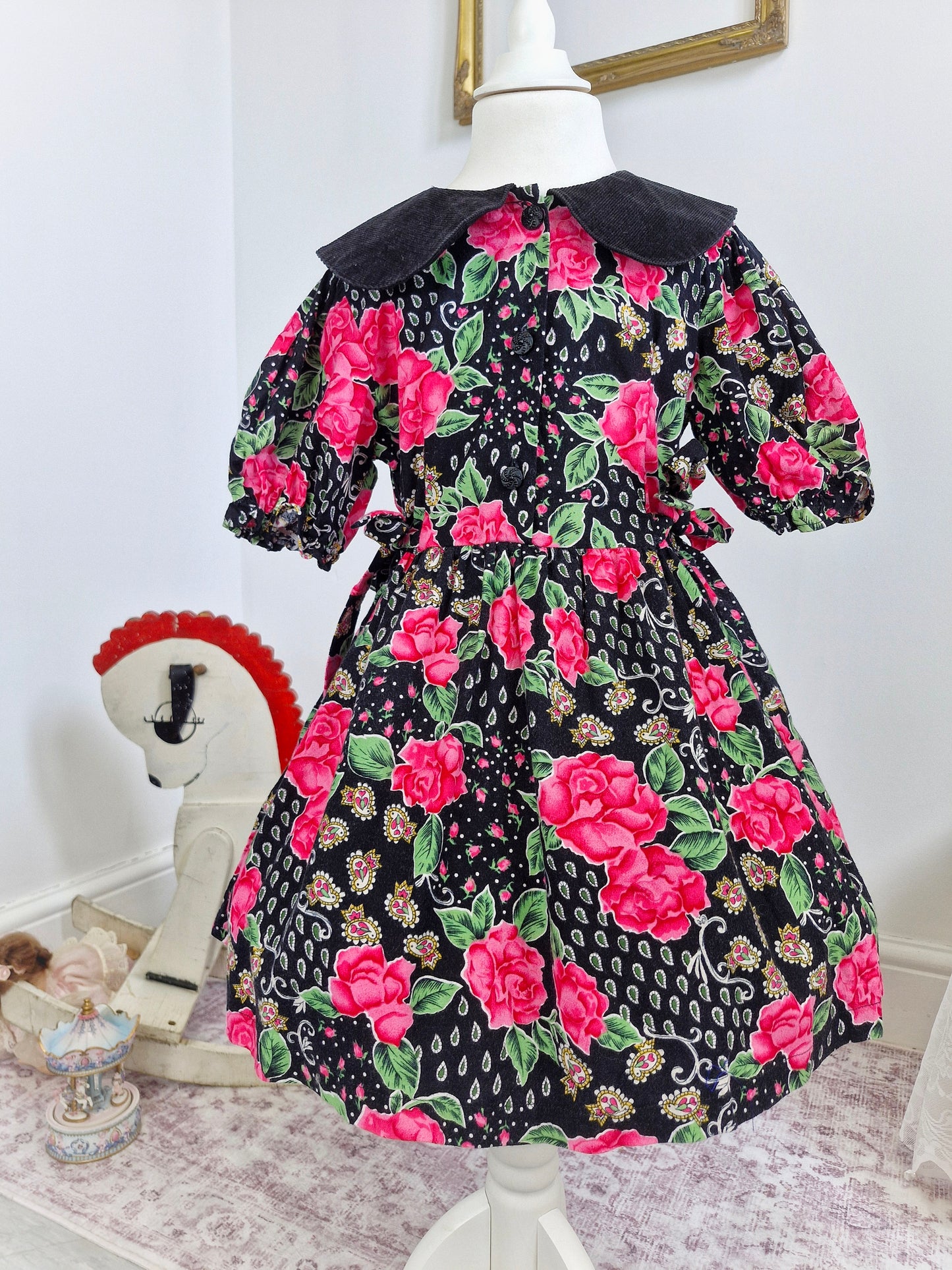 5-6 years. Black dress with pink roses, paisley patterns and a corduroy collar.