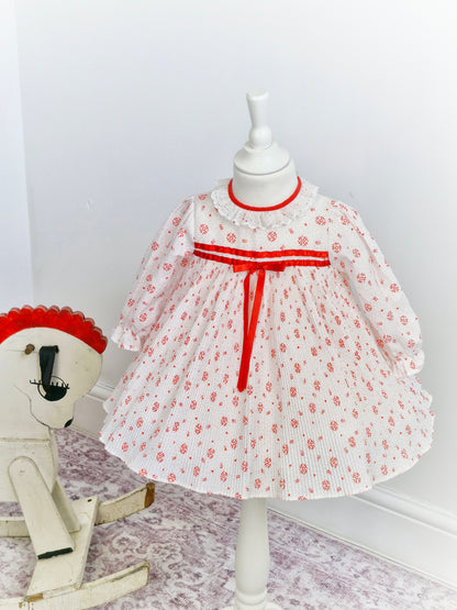 2 years. White dress with mini pleats, red details and ribbon and white lace collar.