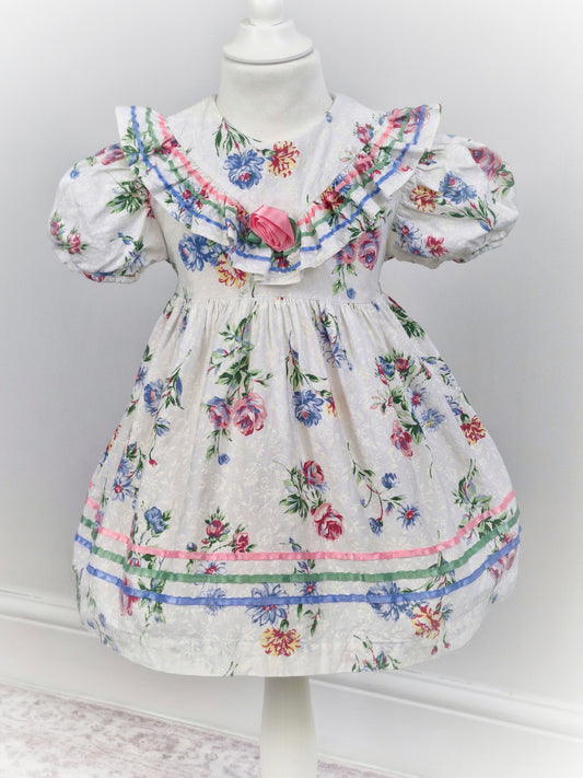 3 years. White dress with floral print, ribbon and rose on ruffled bib