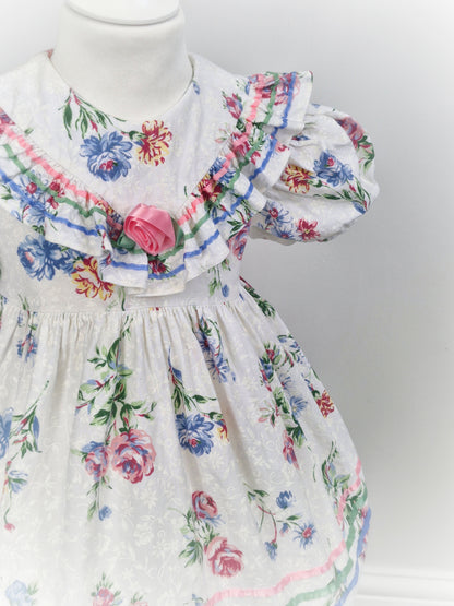 3 years. White dress with floral print, ribbon and rose on ruffled bib