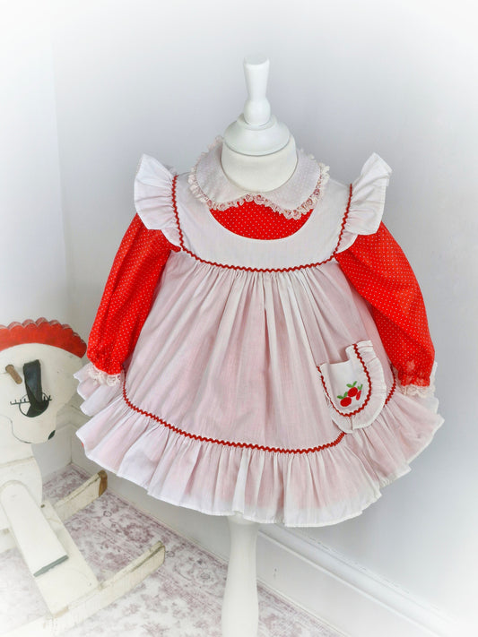 2 years. Red polka dot Bryan with Peter Pan collar and white pinny with flutter sleeves and cherries on pocket.