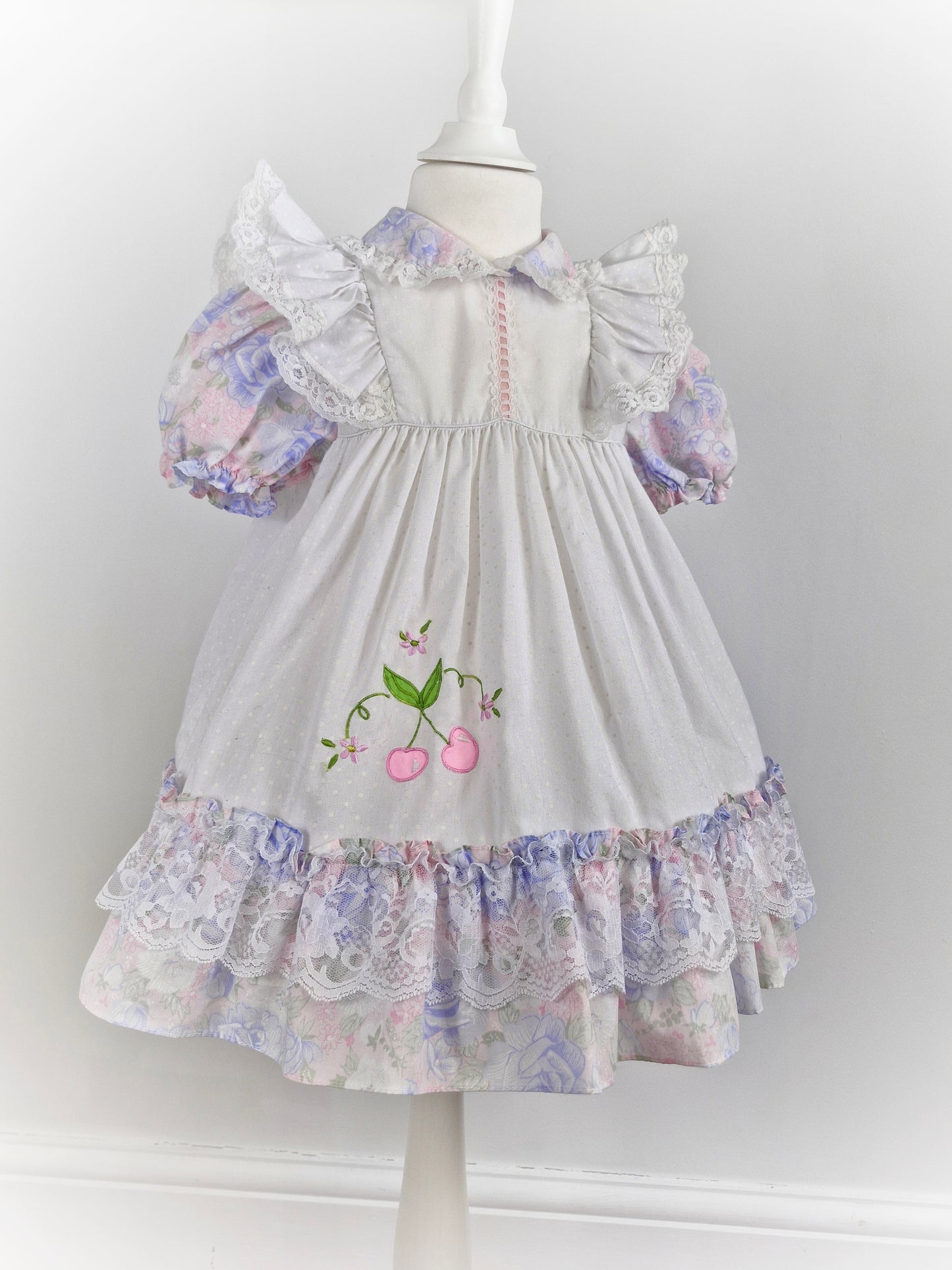 3 years. White dress with pastel flutter sleeves and hem. Cherry applique and lace details