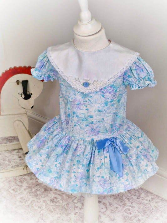 2 years. Pastel coloured drop waist Roanna with white bib and blue ribbon