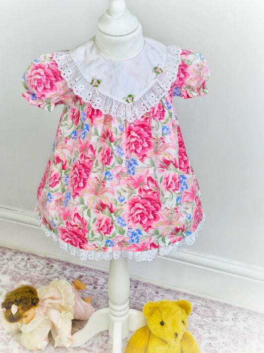 2 years. Pink vintage floral dress with white bib, rosettes and broderie anglais trim