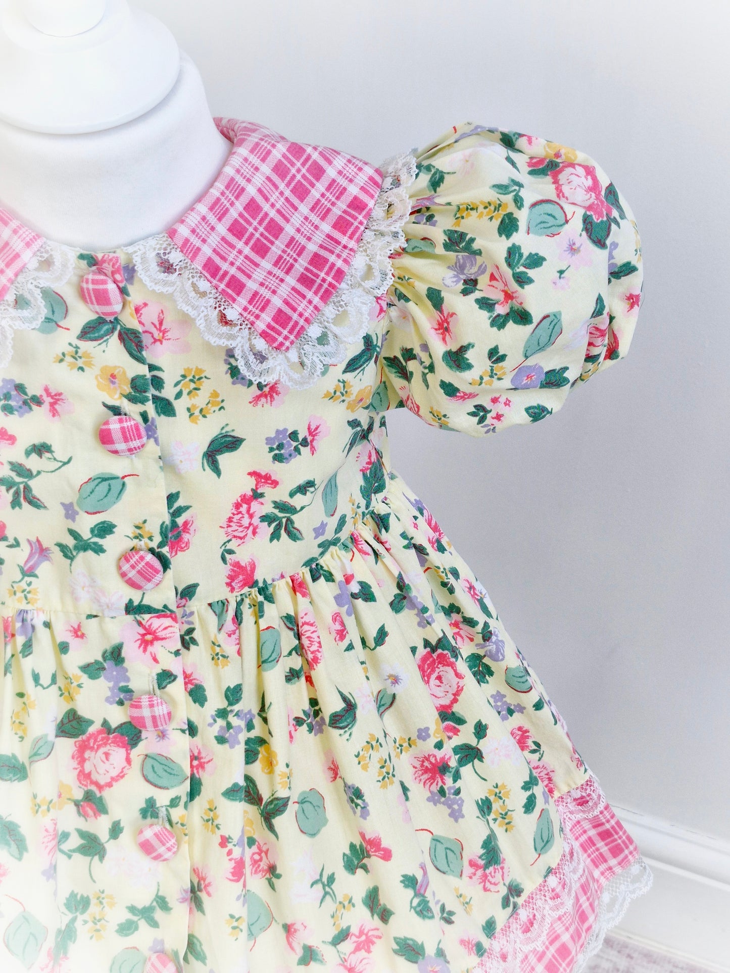 2-3 years. Pale lemon vintage dress by Little Precious with leaf and flower print, pink and white checked collar, hem and buttons. Lace trim