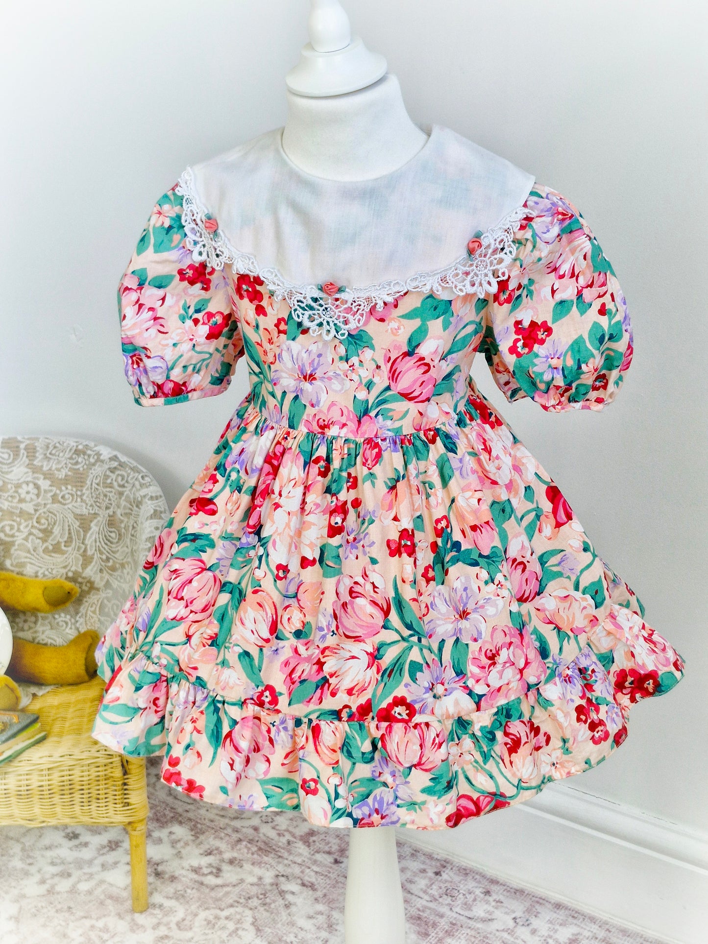 3 years. Peach vintage dress with large flower print, white bib with lace trim and 3 rosettes. Bonnie Jean.