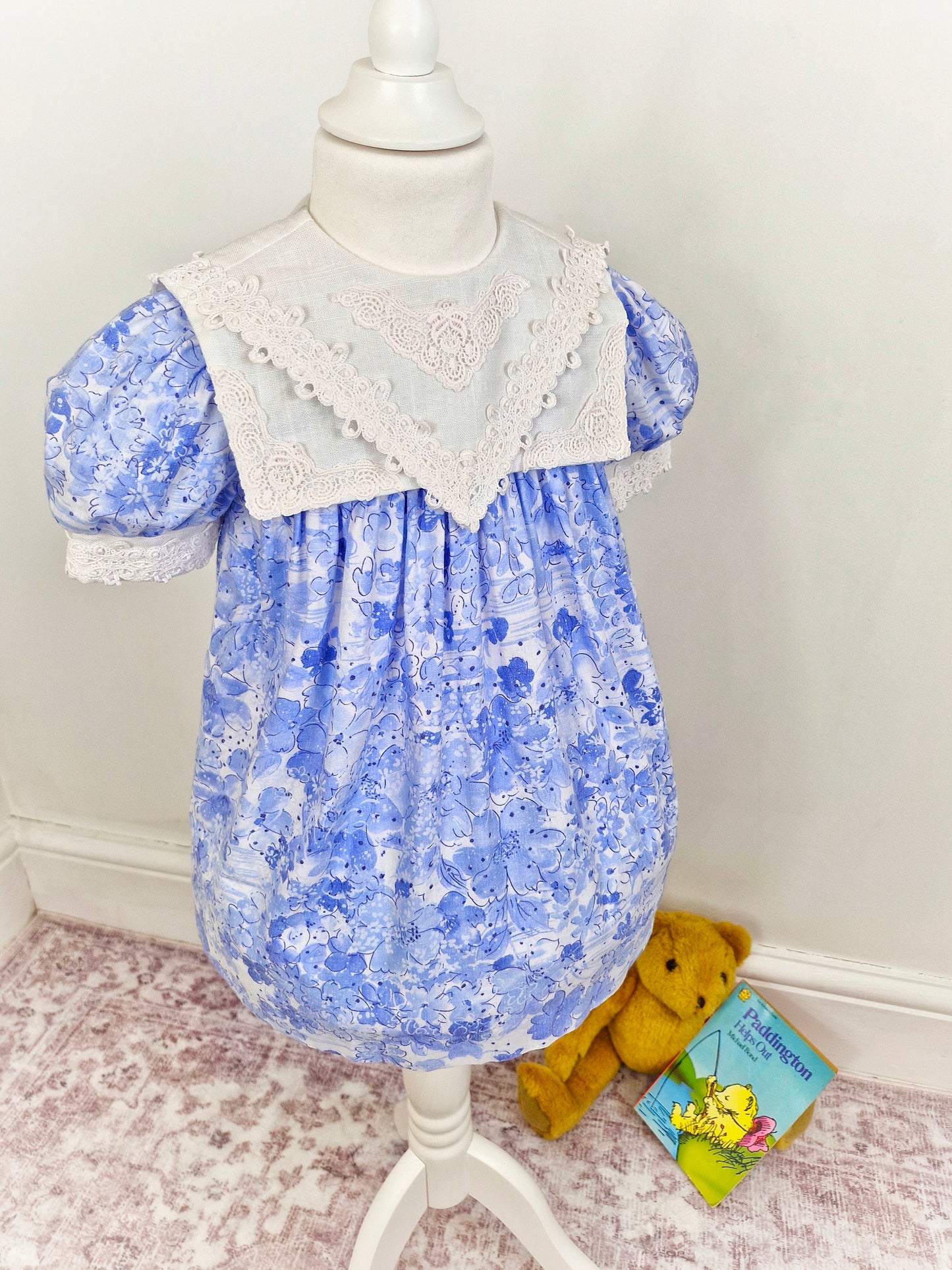 2-3 years. Blue floral dress with white bib and lace details.