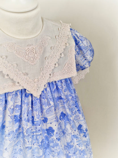 2-3 years. Blue floral dress with white bib and lace details.