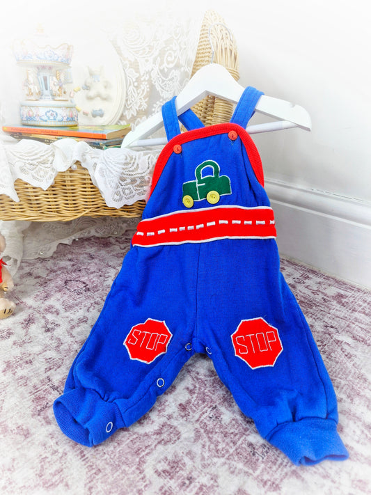 6 months. Blue dungarees with green car and red details