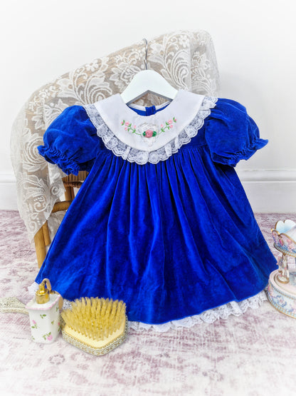 2 years. Royal blue, vintage velvet dress with puff sleeves, white bib and white lace trim. Embroidered flowers