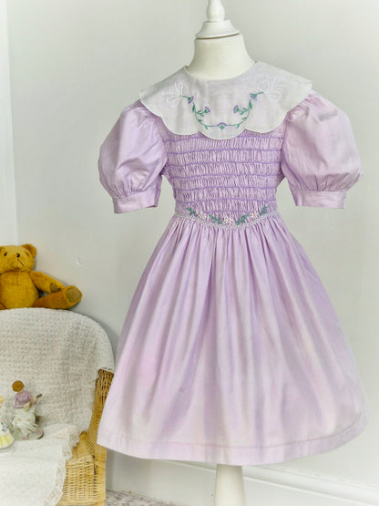 5-6 years. Polly Flinders, vintage lilac smock dress with white bib embroidered with delicate flowers and puff sleeves