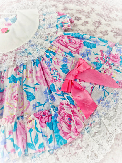 2 years. Vintage Jolene, pink and blue floral dress with white bib and lace, pink bow and rosette