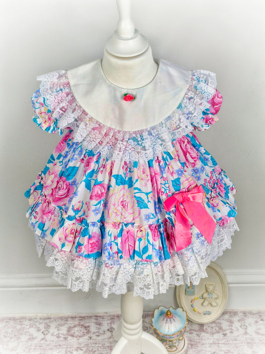 2 years. Vintage Jolene, pink and blue floral dress with white bib and lace, pink bow and rosette