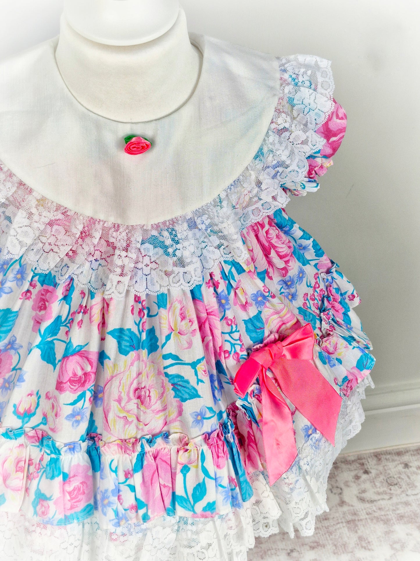 2 years. Vintage Jolene, pink and blue floral dress with white bib and lace, pink bow and rosette