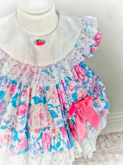 2 years. Vintage Jolene, pink and blue floral dress with white bib and lace, pink bow and rosette