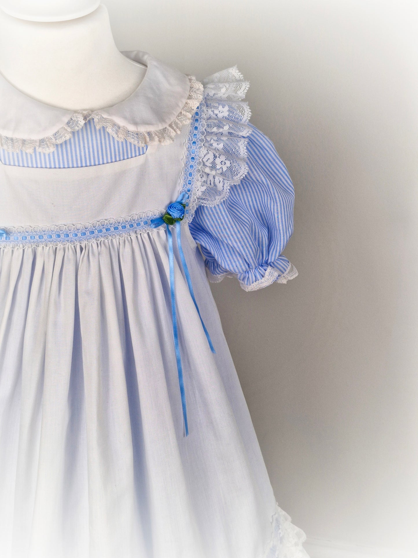 6-7 years. Blue and white candy striped dress with puff sleeves & white apron with flutter shoulders, lace hem and blue ribbons and rosettes
