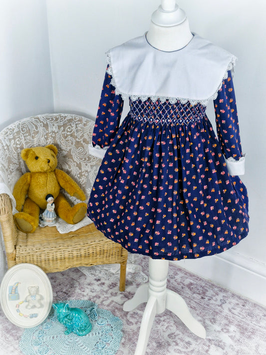 4 years. Navy vintage Polly Flinders dress with white bib, cuffs and smocking and floral print