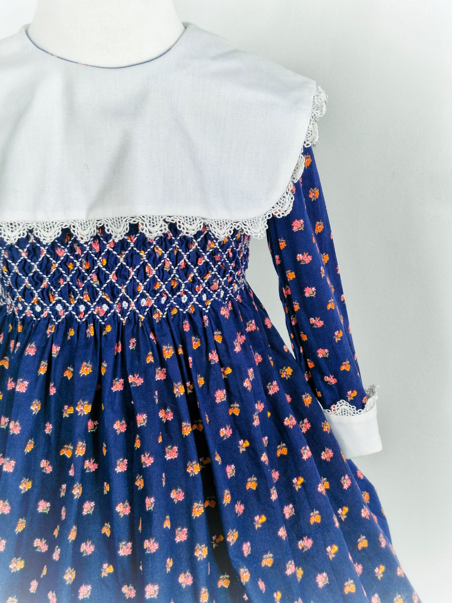 4 years. Navy vintage Polly Flinders dress with white bib, cuffs and smocking and floral print