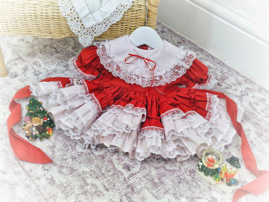 6-12 months. Red Lid'l Dolly with white bib and lace ruffles