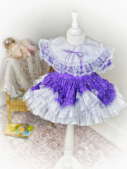 2-3 year. Purple floral Lid'l Dolly with white bib and lace ruffles