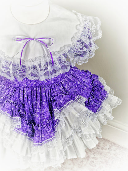 2-3 year. Purple floral Lid'l Dolly with white bib and lace ruffles