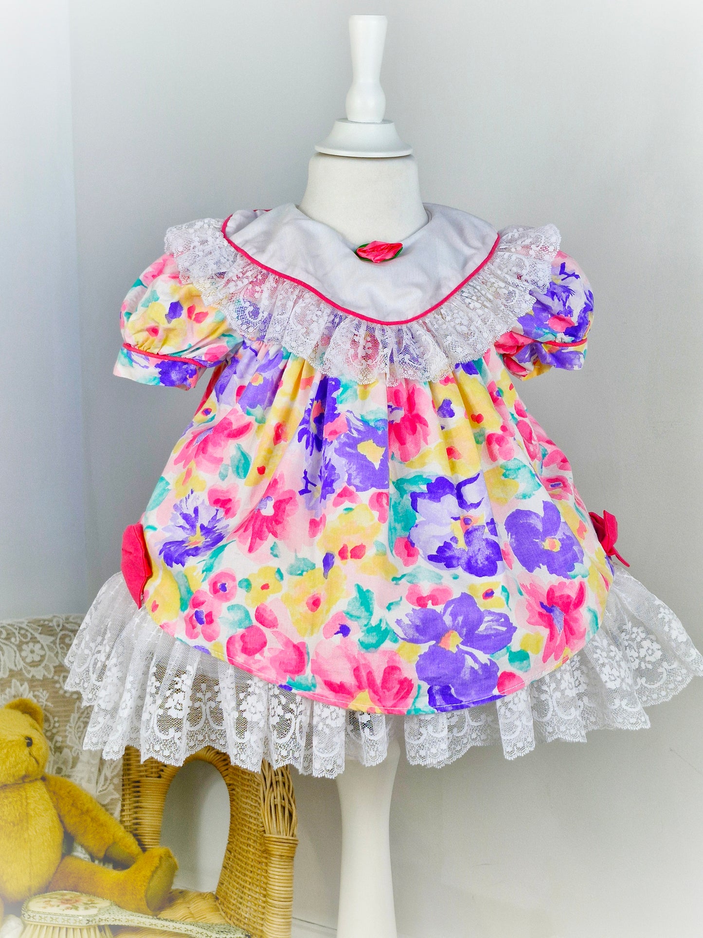 2 years. Bright floral vintage dress by Jolene, white bib with lace trim and hem, pink bows and rosette