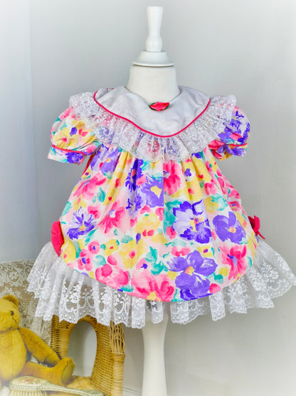 2 years. Bright floral vintage dress by Jolene, white bib with lace trim and hem, pink bows and rosette