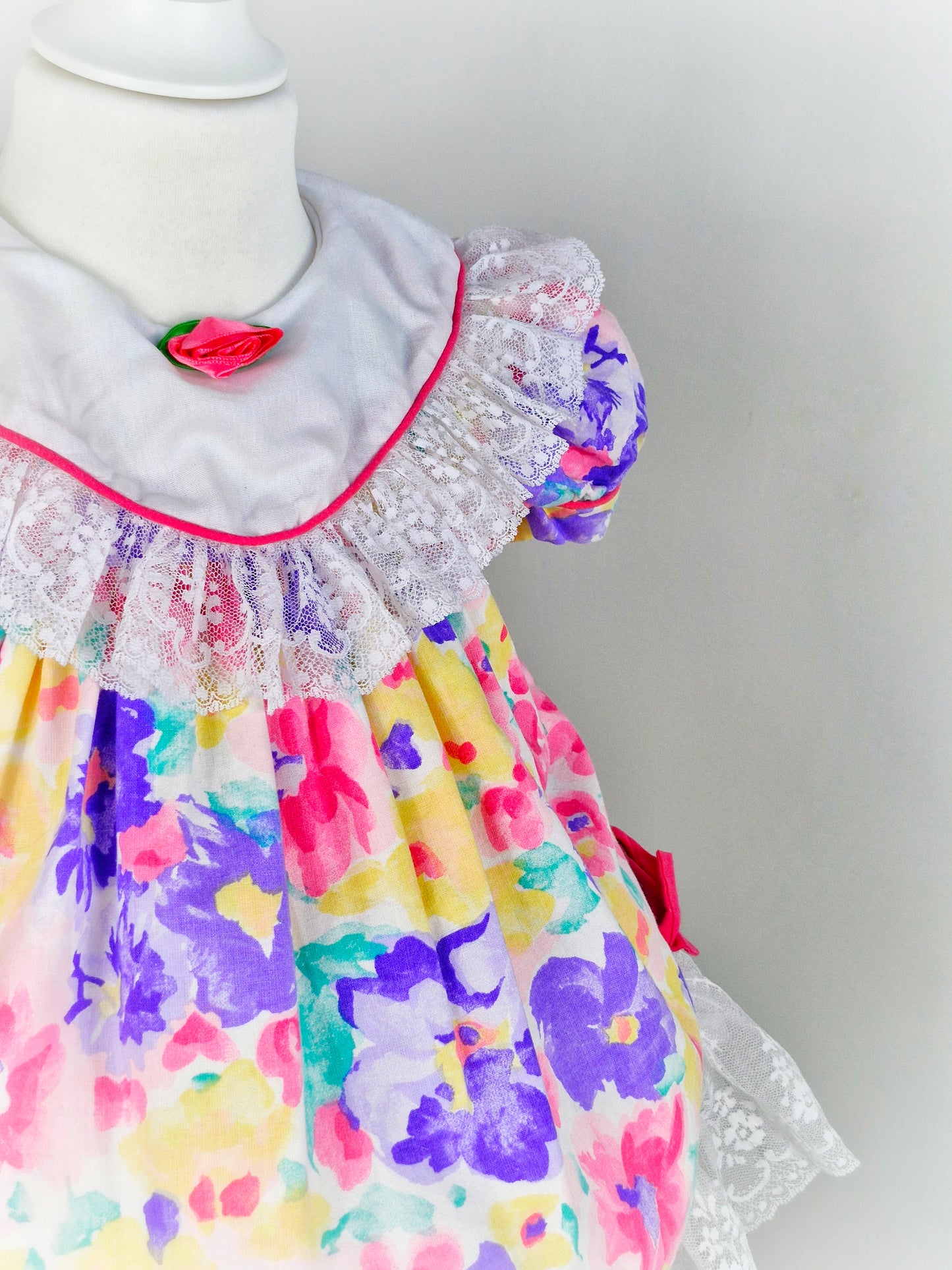 2 years. Bright floral vintage dress by Jolene, white bib with lace trim and hem, pink bows and rosette